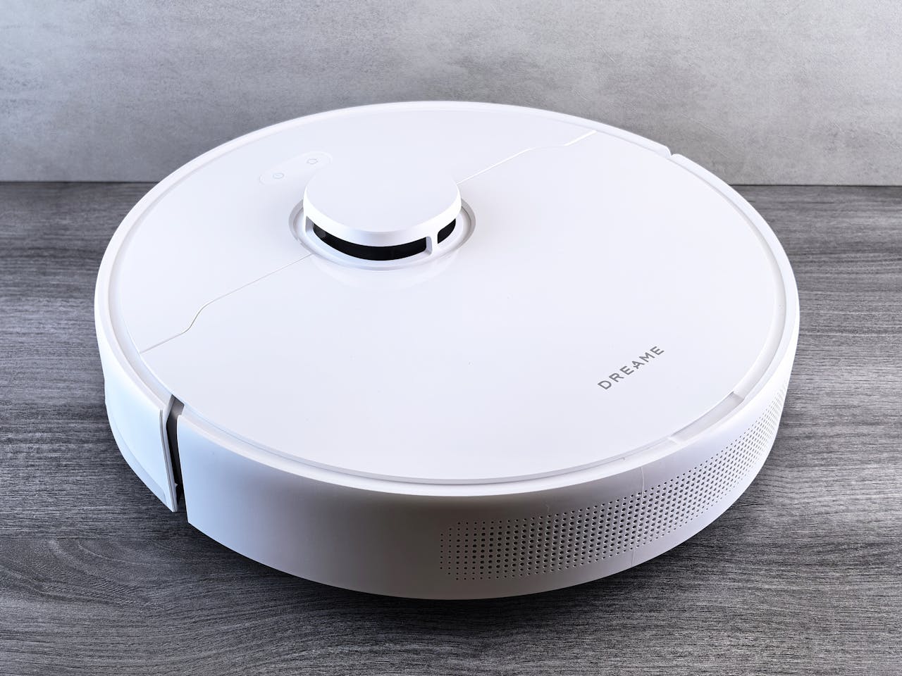 High-angle view of a sleek white robotic vacuum cleaner on a wooden floor, perfect for smart home setups.